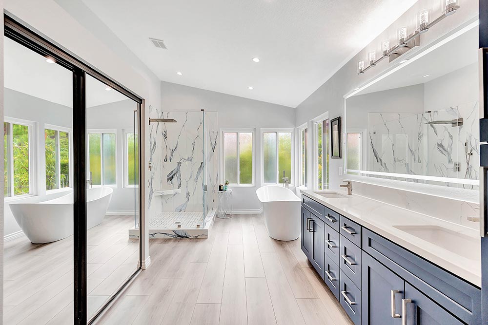 Finished bathroom remodel in Laguna Hills with blue vanities, freestanding tub, and marble-look walk-in shower