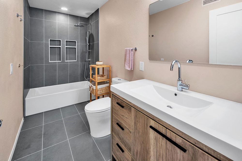 Modern bathroom in Carlsbad with dark tile walls, wood vanity, rain shower, and built-in niches
