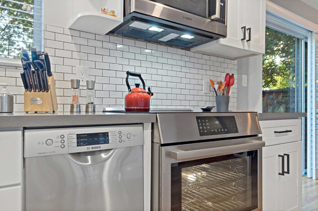 Energy Star stainless steel dishwasher and electric range in a sustainable Laguna Niguel kitchen remodel with white subway tile backsplash and white shaker cabinets.