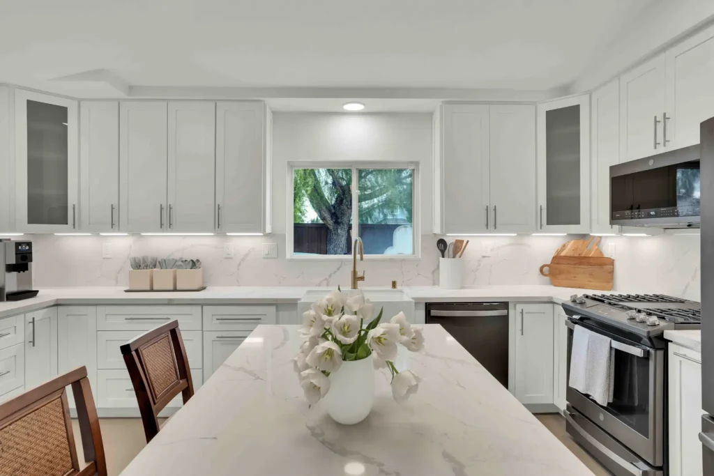 Modern white kitchen remodel with marble-look quartz island, pendant lights, and stainless range hood