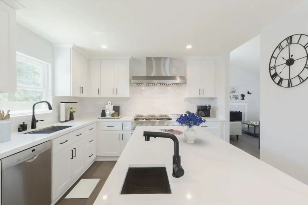 White shaker kitchen remodel with quartz island, black faucet, and open-plan layout with wall clock
