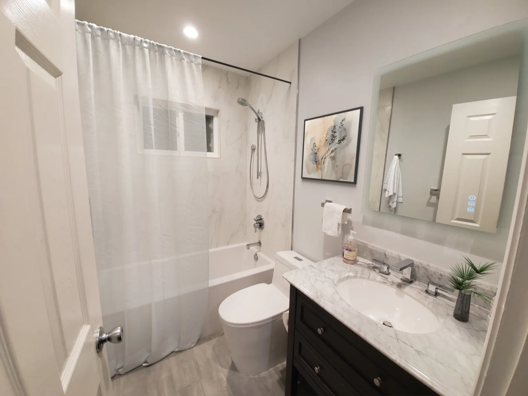 Lake Forest bathroom remodel with tub/shower combo, marble-look wall tile, and black vanity with marble top.