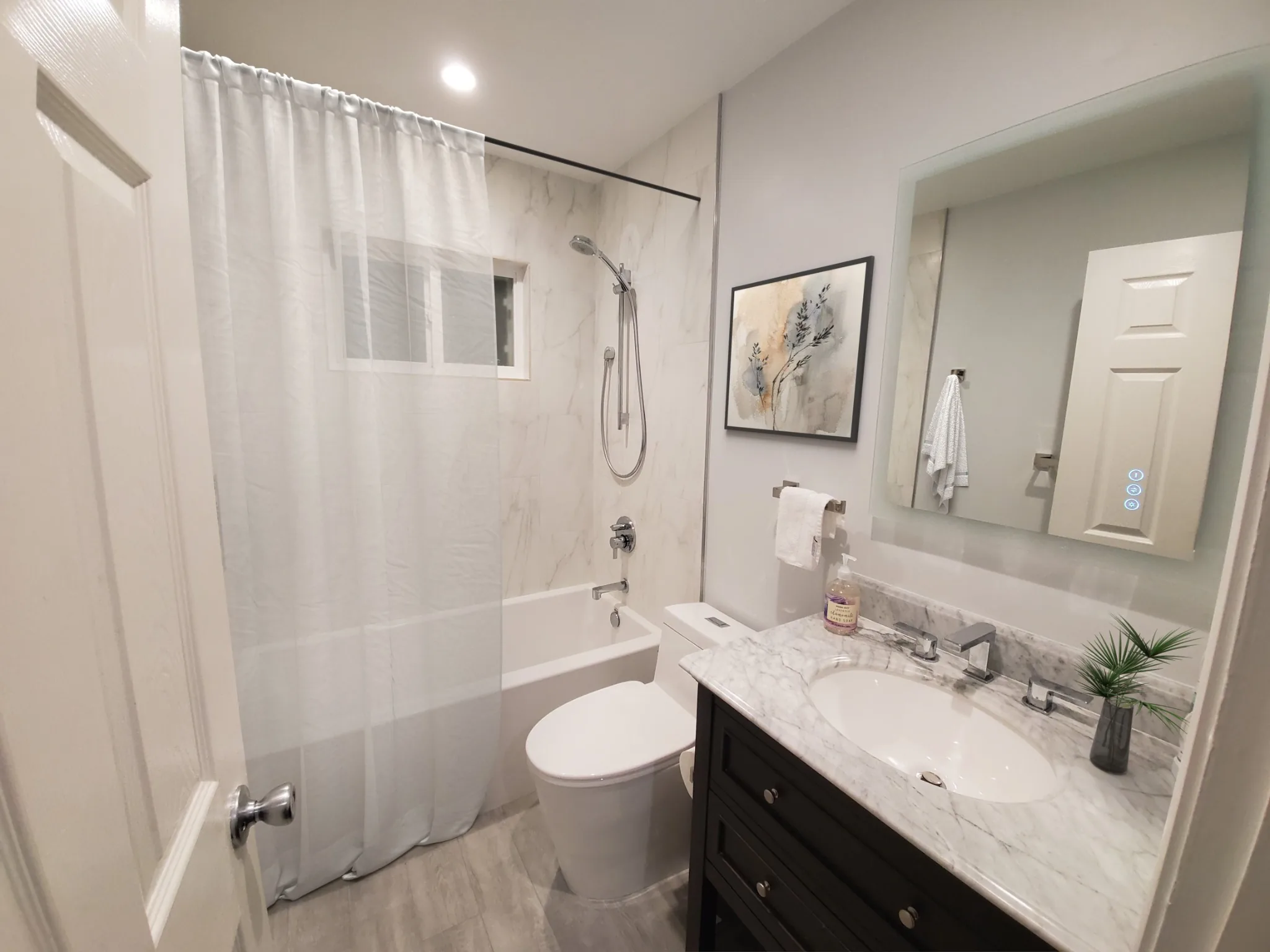Lake Forest bathroom remodel with tub/shower combo, marble-look wall tile, and black vanity with marble top.