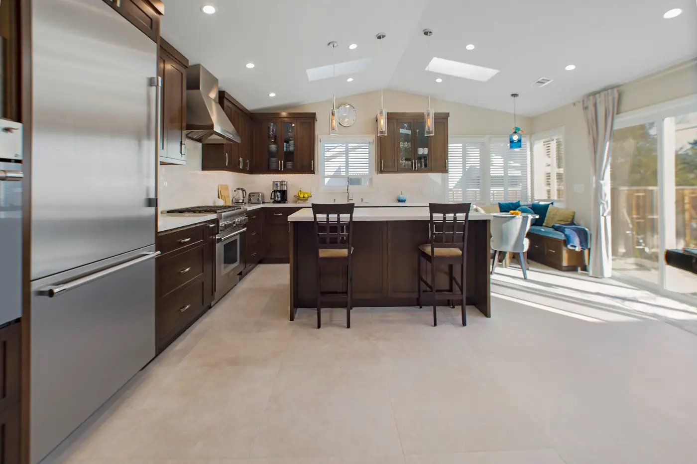 A contemporary custom kitchen in Irvine featuring dark cabinetry, a large island with seating, hardwood floors, and stainless steel appliances in an open, spacious layout.