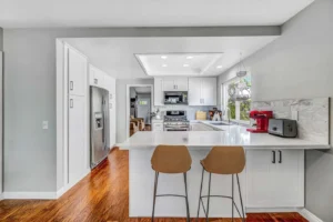 A bright, renovated Irvine kitchen featuring white shaker cabinets, quartz countertops, a soft gray marble backsplash, and a sink relocated to the center of the window for an open, airy feel.