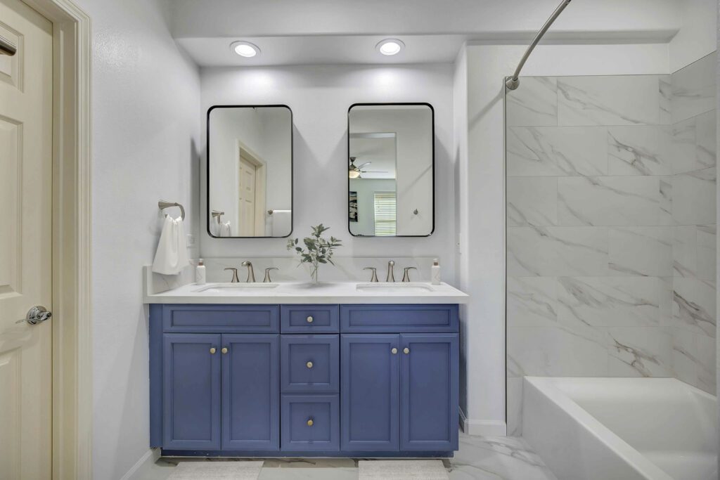 Irvine bathroom remodel with blue double vanity, white quartz countertops, brushed nickel fixtures, and marble-look tile shower by USA Home Remodeling