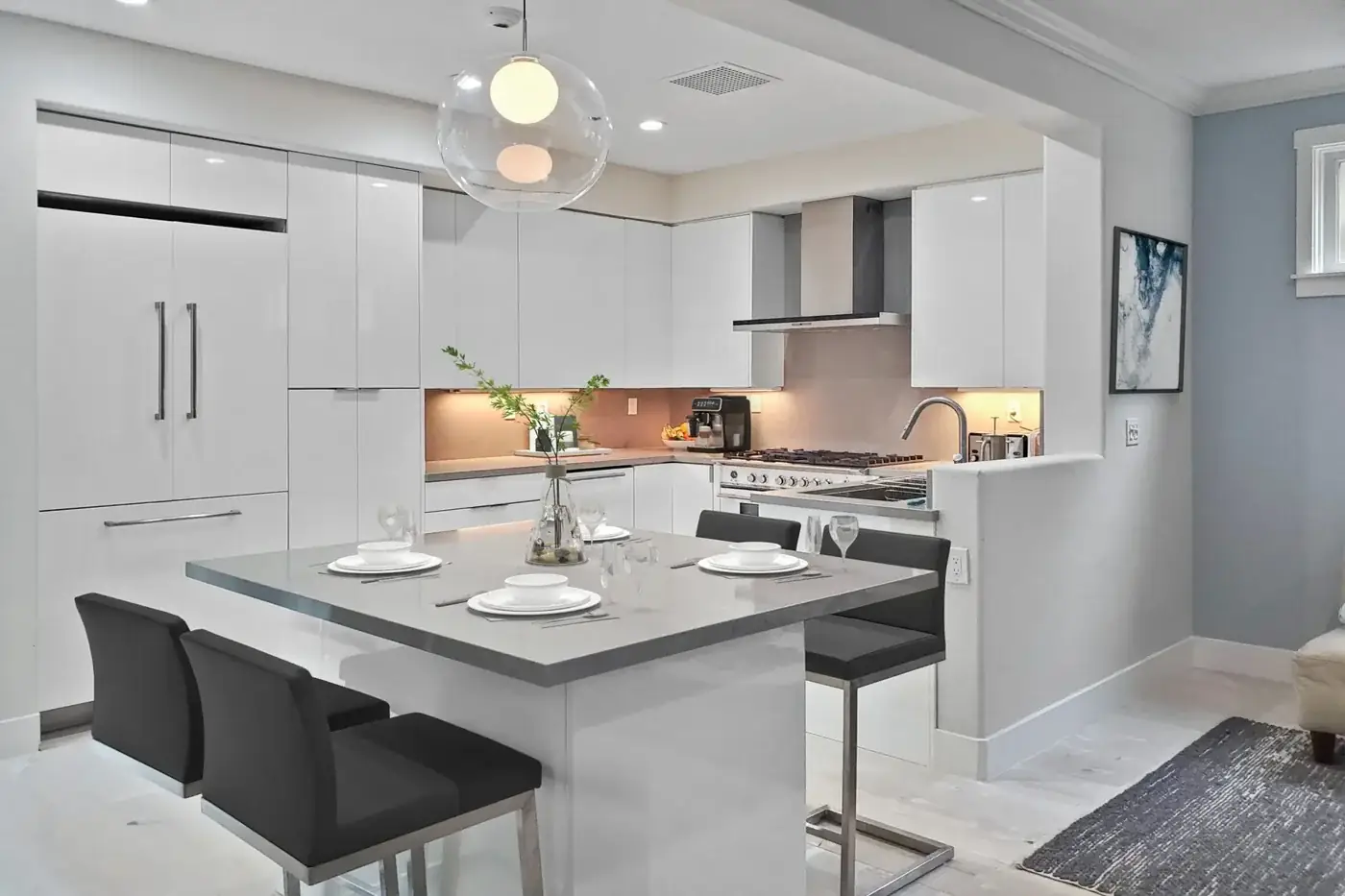 Laguna Hills kitchen remodel - Sleek white flat-panel cabinets, globe pendant, quartz dining peninsula, modern