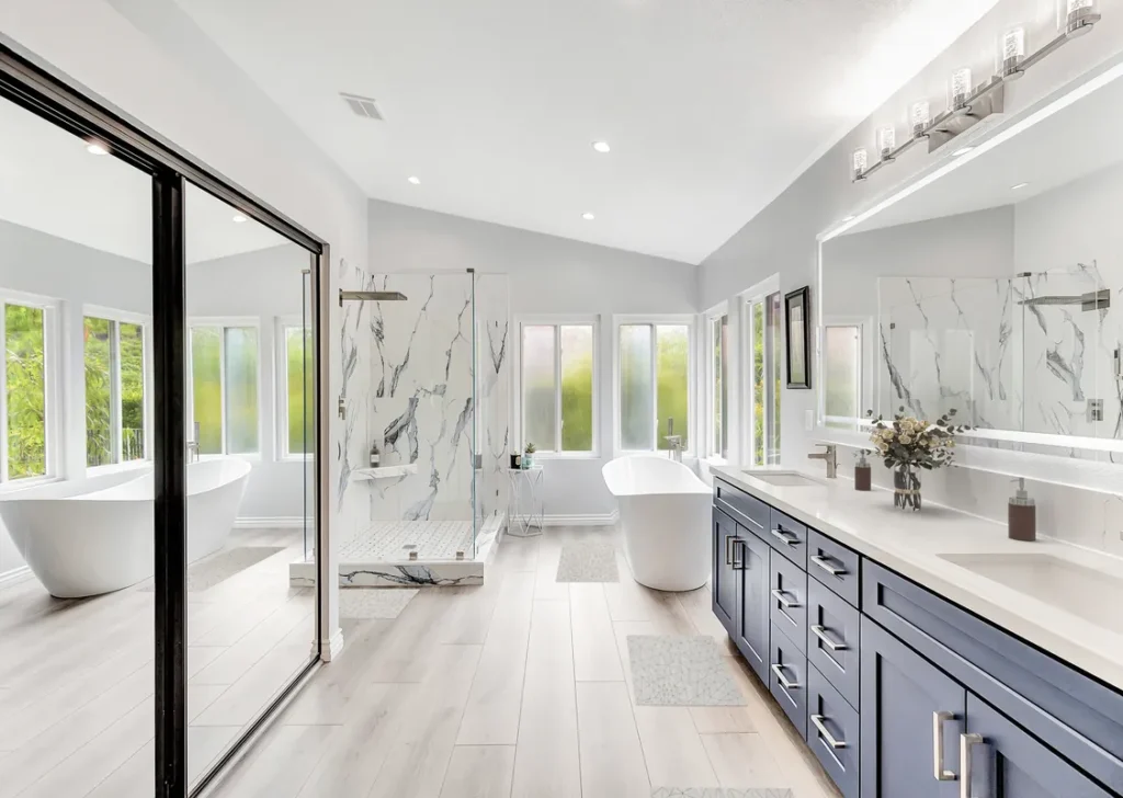 Laguna Hills master bathroom remodel after photo featuring a freestanding soaking tub, a navy double vanity with quartz countertops, and a Calacatta marble walk-in shower with frameless glass