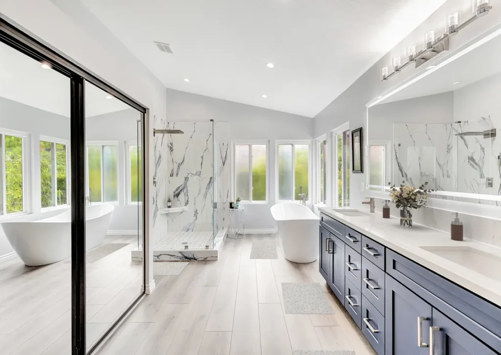 Santa Ana master bathroom remodel after photo featuring a freestanding soaking tub, a navy double vanity with quartz countertops, and a Calacatta marble walk-in shower with frameless glass