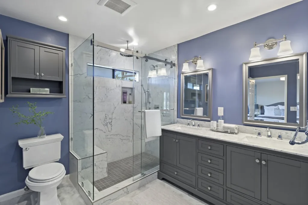Orange County guest bathroom remodel after photo featuring soft periwinkle blue walls, a dark stained shaker vanity, polished sconces, and a Carrara marble walk-in shower