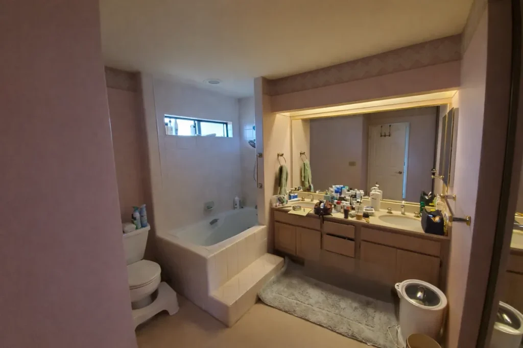 Orange County guest bathroom before remodel with dated pink walls, an older vanity, and a standard tub-shower