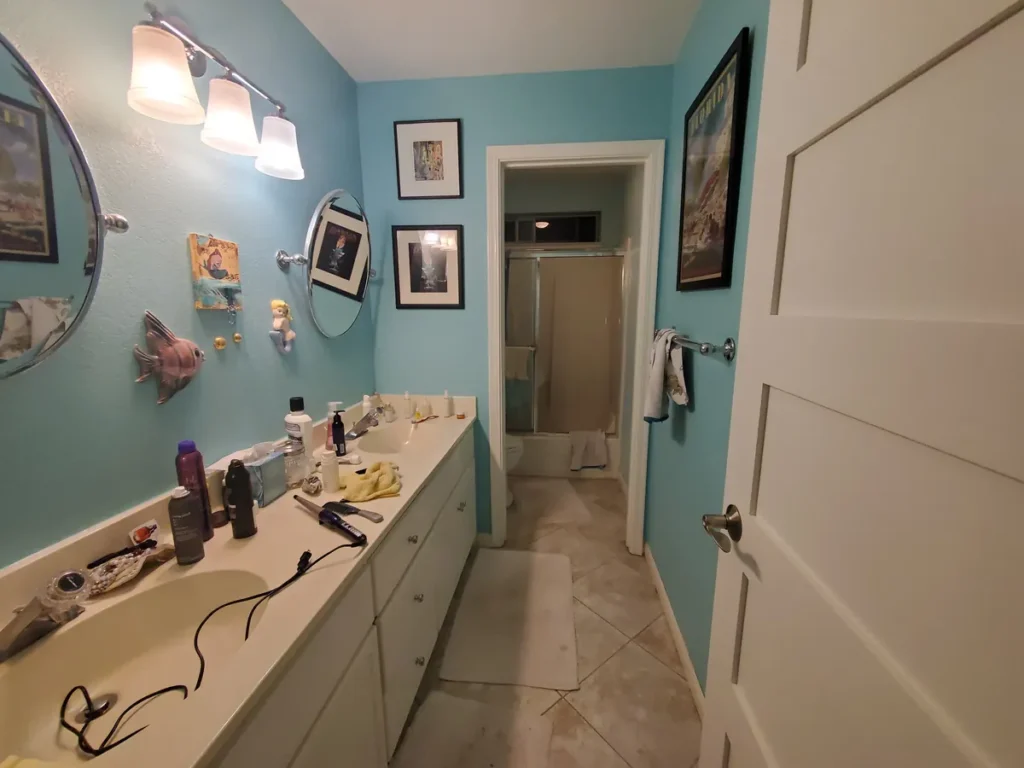 Laguna Hills guest bathroom before remodel with dated teal walls, a double vanity with round mirrors, and older fixtures