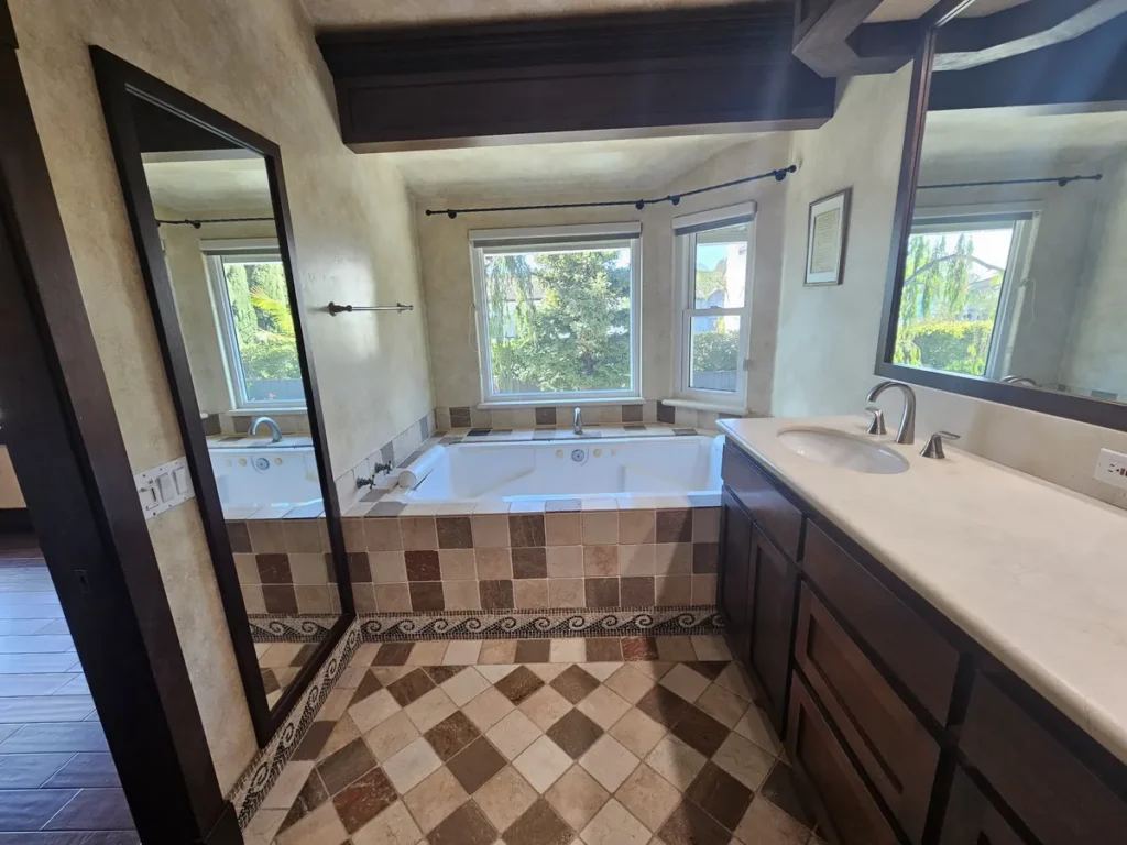 San Juan Capistrano master bathroom before remodel with a dark walnut Spanish Mediterranean tub area, a built-in jacuzzi, and a heavy mosaic tile floor