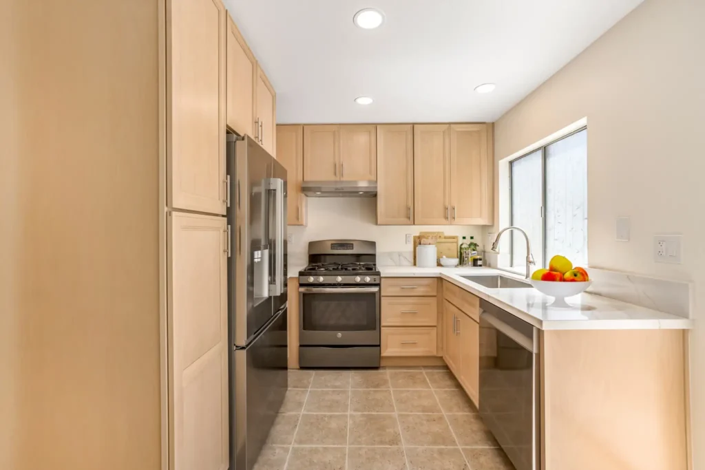 Remodeled Irvine kitchen with natural wood cabinets, white quartz countertops, stainless steel appliances, and a sink beneath the window.