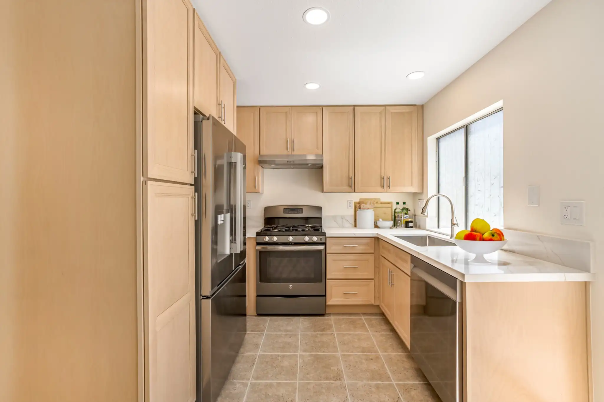 Remodeled Irvine kitchen with natural wood cabinets, white quartz countertops, stainless steel appliances, and a sink beneath the window.