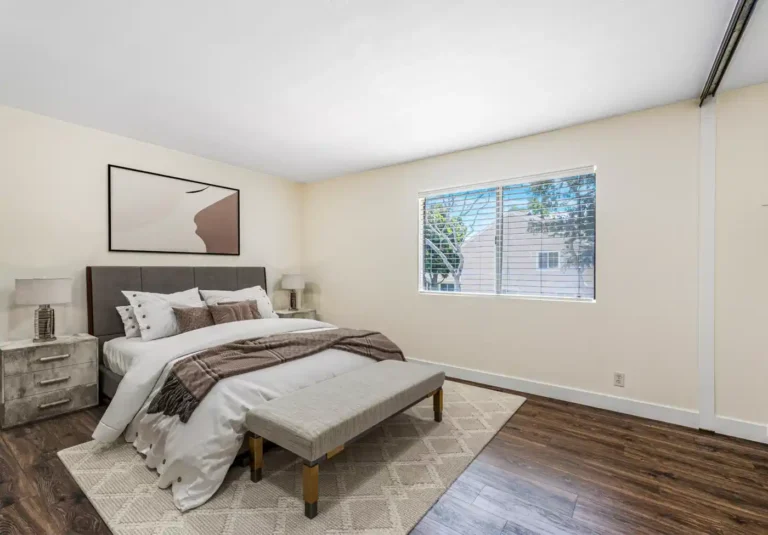 Irvine guest bedroom with an upholstered bed, neutral bedding, bench, large window, and dark wood flooring.