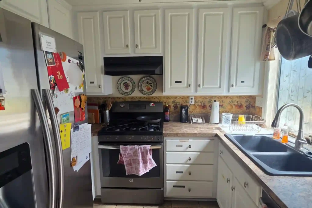 Before photo of an Irvine kitchen with a black gas range, decorative plates, worn laminate counters, and a dark double sink.