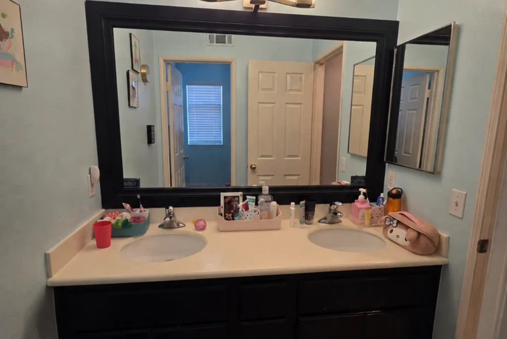 Outdated double-sink bathroom vanity before remodel with black cabinets and large framed mirror