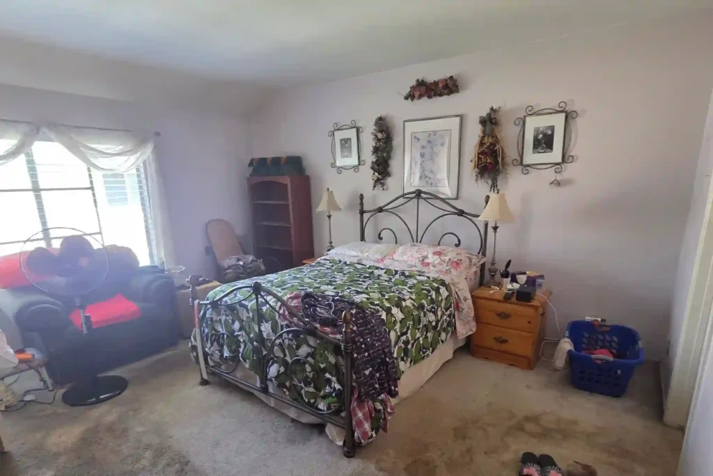 Before photo of an Irvine primary bedroom with carpet flooring, a metal bed frame, mismatched furniture, and dated decor.
