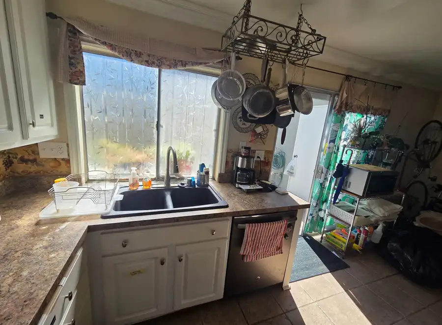 Dated Irvine kitchen before remodeling, with a hanging pot rack, floral valance, and worn laminate countertops by the sink.