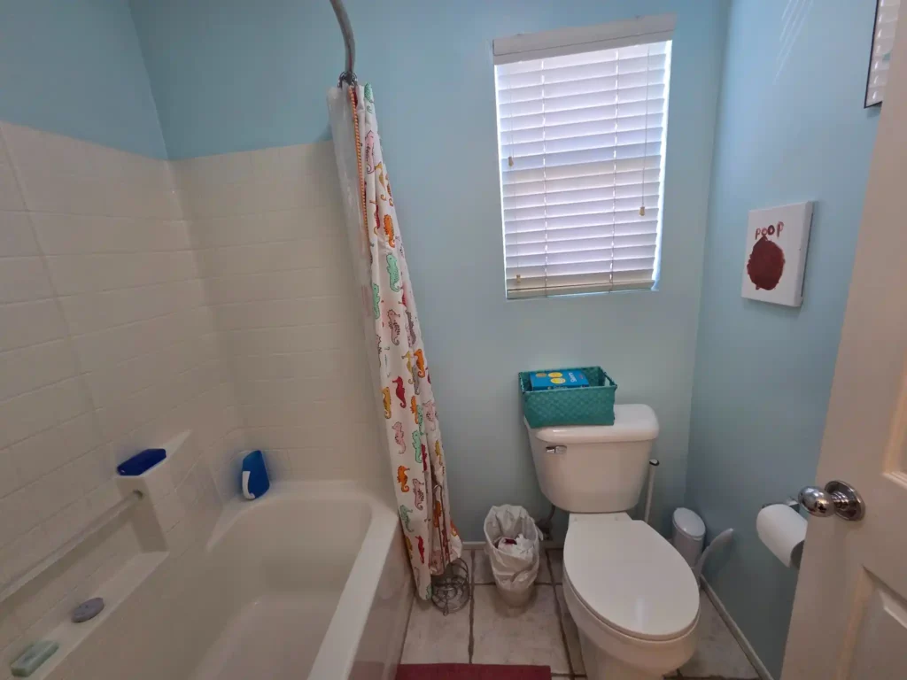 Outdated bathroom before remodel with tub shower combo, toilet, and blue walls