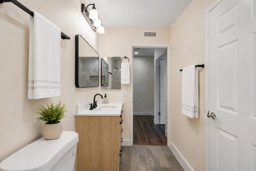 Oak vanity with white quartz countertop, matte black faucet, and a black-framed mirror in a remodeled Irvine bathroom.