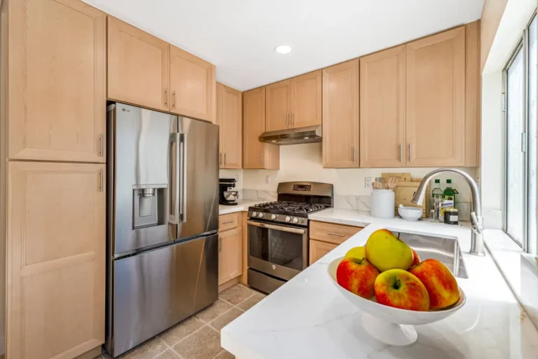Irvine kitchen with natural wood cabinets, stainless steel refrigerator and range, quartz counters, and window-side sink.