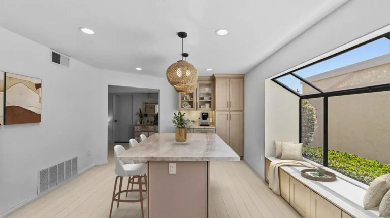 Long stone island beside a built-in window bench in a bright remodeled kitchen in Carlsbad.