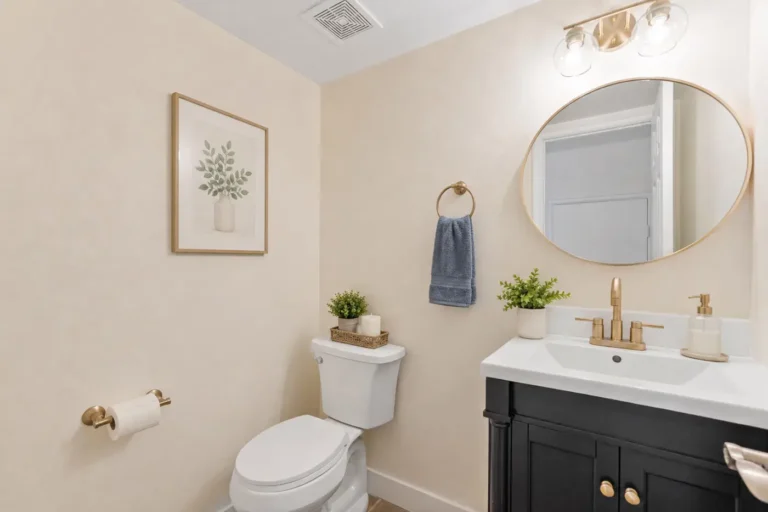 Irvine powder room with a black vanity, white countertop, round gold mirror, brushed gold fixtures, and neutral decor.
