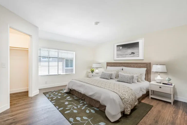 Bright Irvine primary bedroom with wood flooring, upholstered bed, white nightstands, neutral bedding, and walk-in closet.