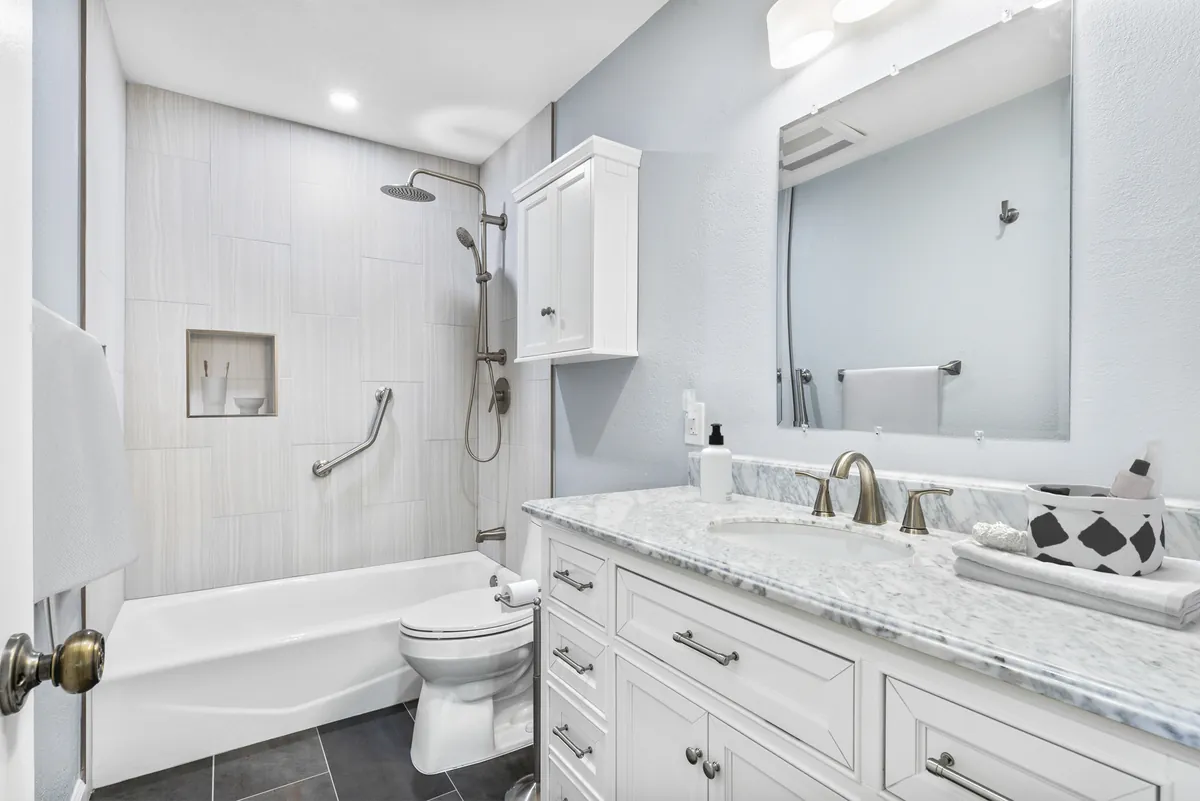 Brea guest bathroom renovation — soft blue-gray walls, a white traditional vanity, and a stone-look tile walk-in shower