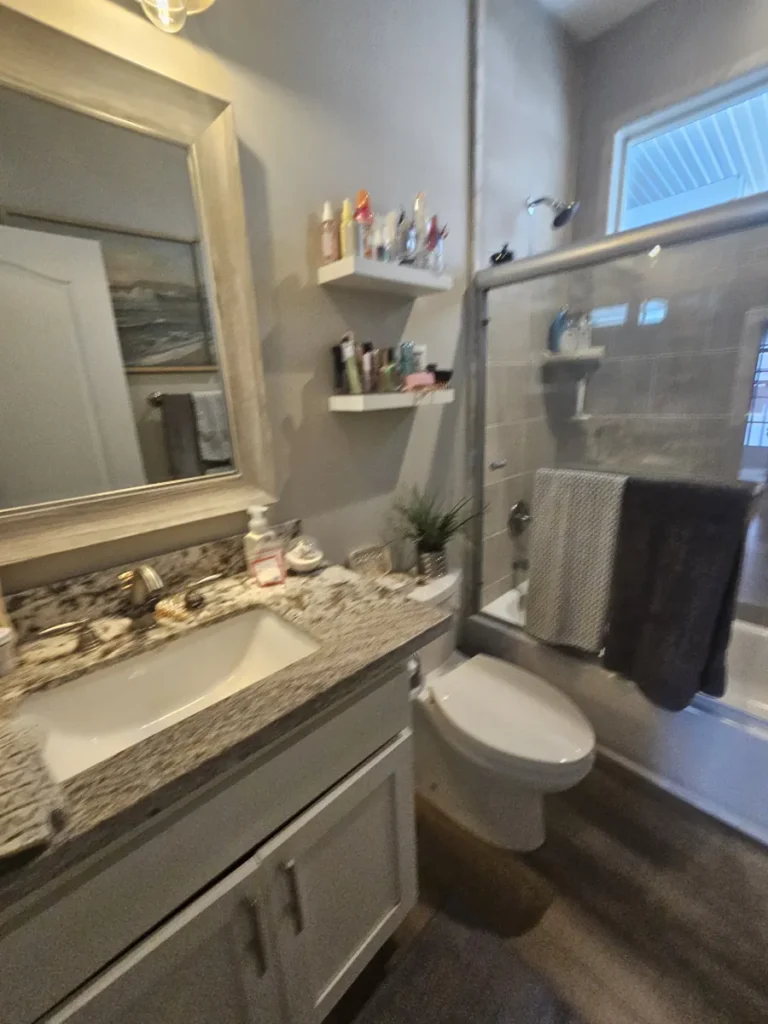 Villa Park guest bathroom before remodel with a brown granite countertop, framed glass tub doors, and dated cluttered finishes