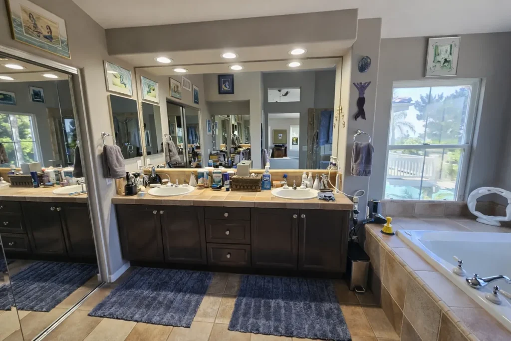 Laguna Woods master bathroom before remodel with a dark cluttered wood vanity, tile countertop, and dated finishes