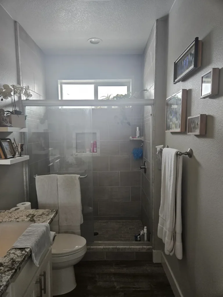 Buena Park master bathroom before remodel with dated gray tile, framed glass shower doors, and a narrow walk-in shower layout