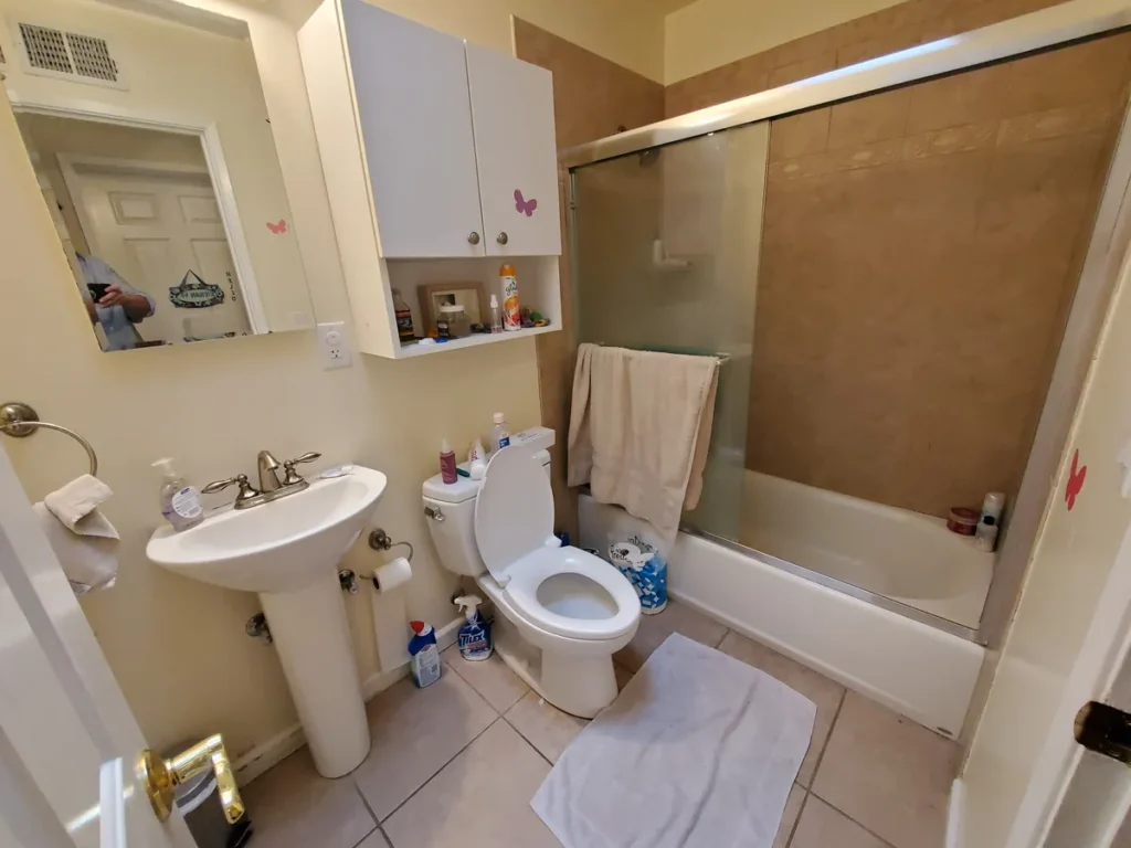 Yorba Linda guest bathroom before remodel with a dated pedestal sink, cream walls, and a beige tub surround