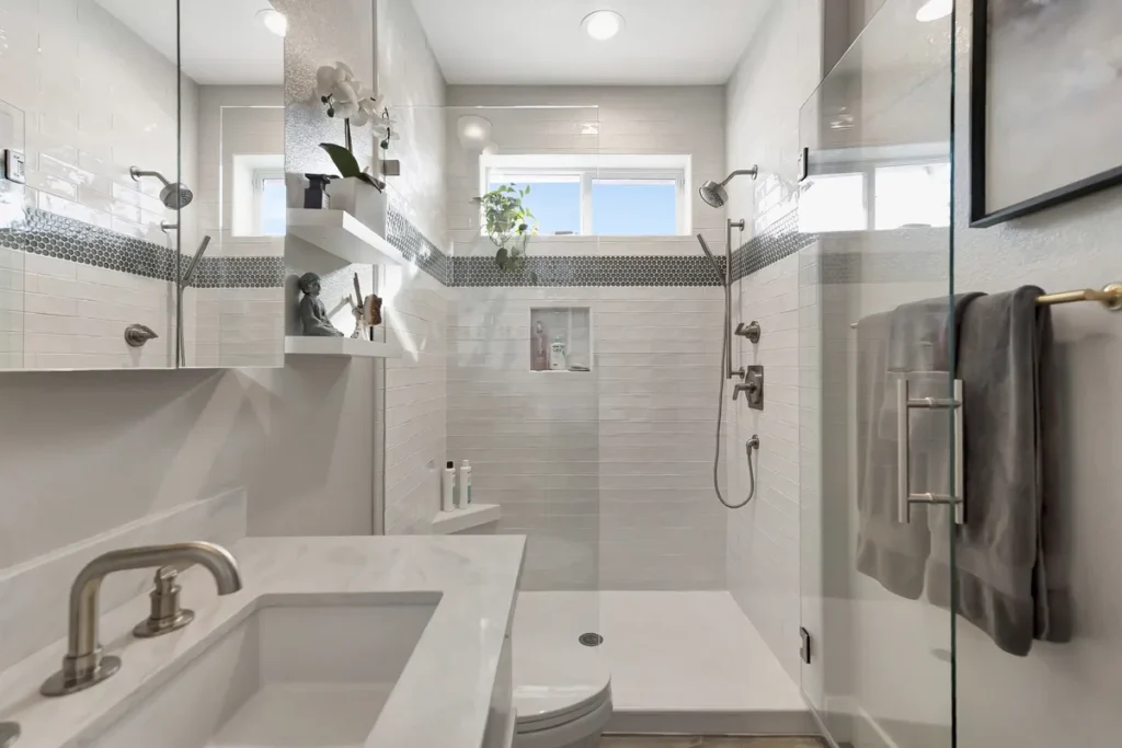 Leucadia master bathroom remodel after photo featuring white subway tile with a penny mosaic accent band, frameless glass, and dual shower heads