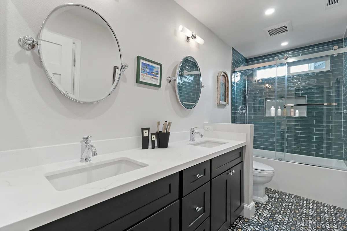 Laguna Woods guest bathroom remodel — round mirrors, a dark vanity, and teal glass subway tile shower