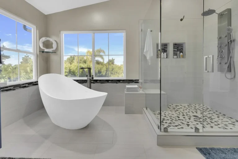 Freestanding slipper tub beside a frameless glass shower with pebble mosaic floor in a Carlsbad primary bathroom
