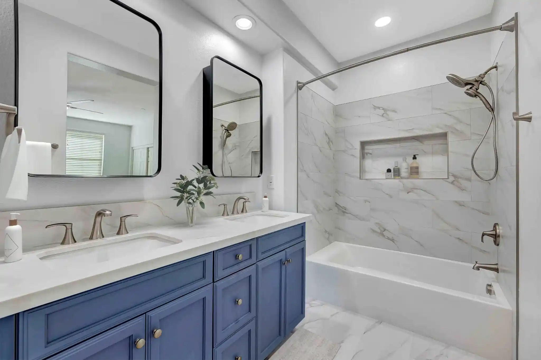 Irvine bathroom remodel with blue double vanity and marble-look tub/shower surround with large inset niche.