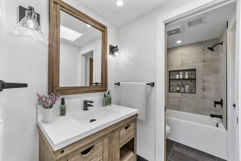 Warm wood vanity with a quartz top beside a tiled tub and shower combo in a Santa Ana bathroom remodel