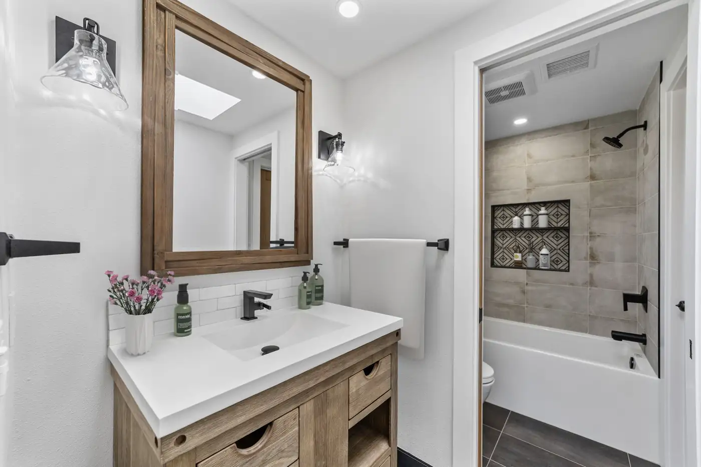 Warm wood vanity with a quartz top beside a tiled tub and shower combo in a Santa Ana bathroom remodel