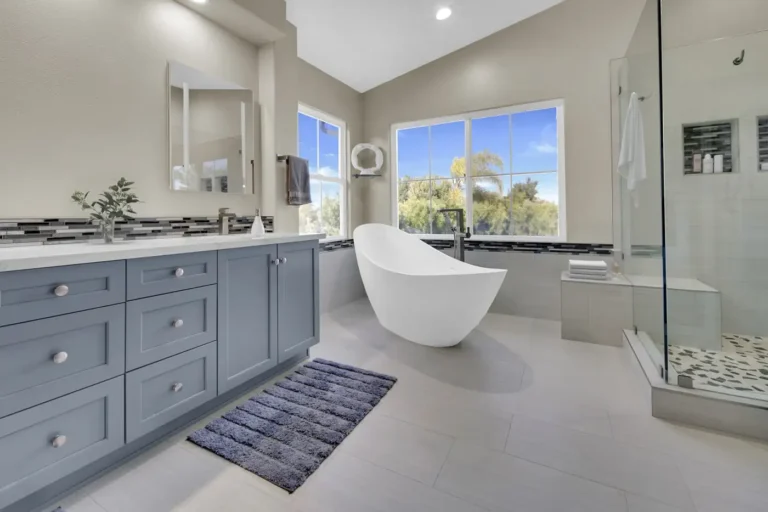 Dusty blue shaker double vanity with white quartz countertop facing a freestanding tub in a Carlsbad bathroom remodel