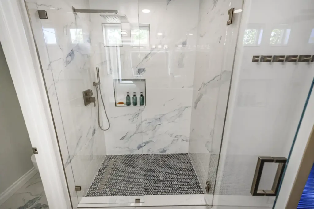 Frameless glass walk-in shower with marble-look tile and a hexagon mosaic floor in Irvine, California
