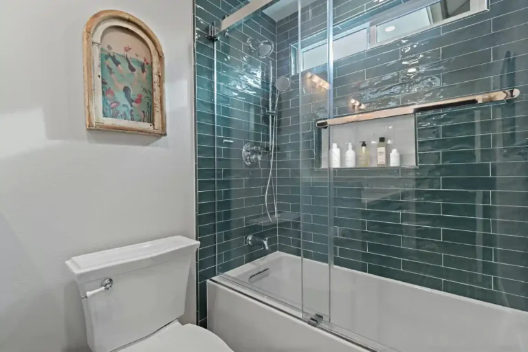 Teal glass subway tile tub shower with sliding glass doors and a recessed niche in an Anaheim guest bathroom.