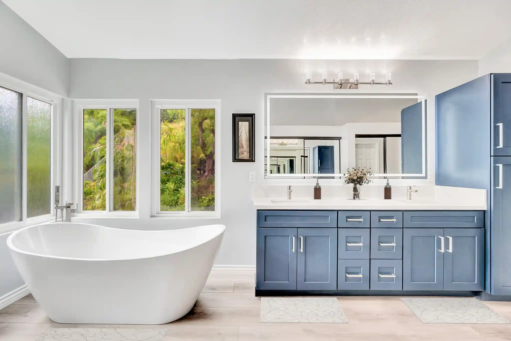 Blue double vanity with quartz countertop opposite a freestanding tub in a Laguna Hills bathroom.