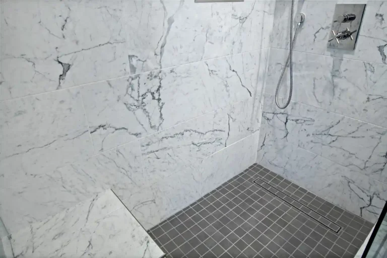 Marble-tile walk‑in shower with bench and linear drain.