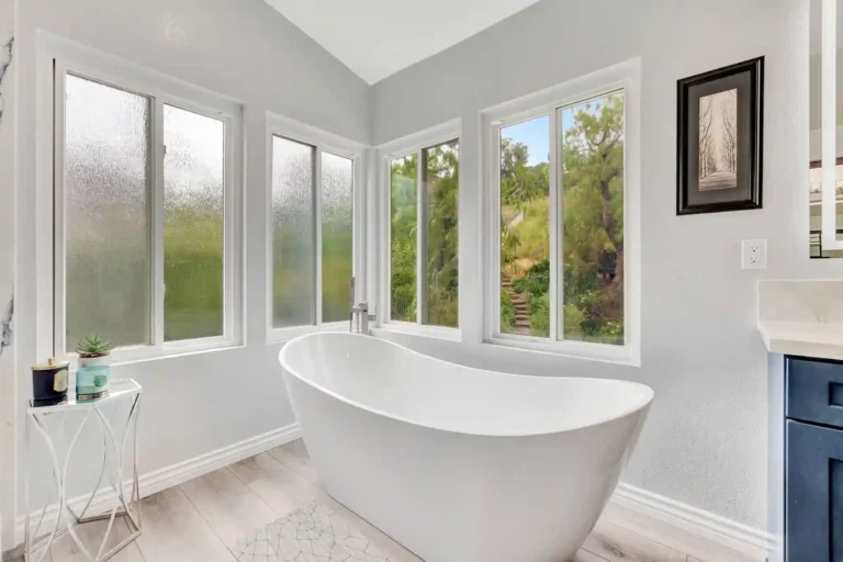 White freestanding soaking tub in a window-lined corner of a Laguna Hills primary bathroom.