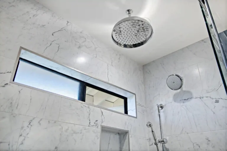Rain shower and handheld in a marble‑tile shower with clerestory window.