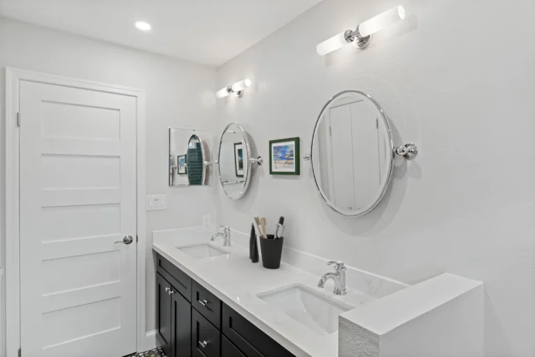 Two pivoting chrome oval mirrors above a white quartz double vanity in a remodeled Anaheim guest bathroom.