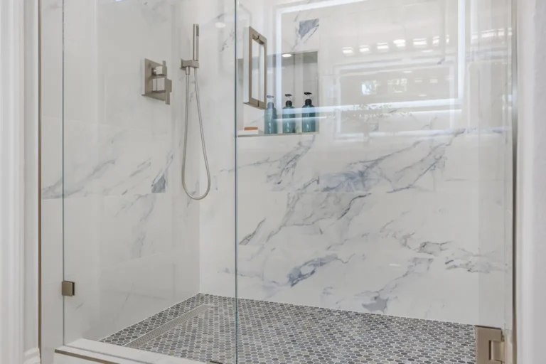 Marble-look tiled shower with a hexagon mosaic floor in a remodeled bathroom in Irvine, California